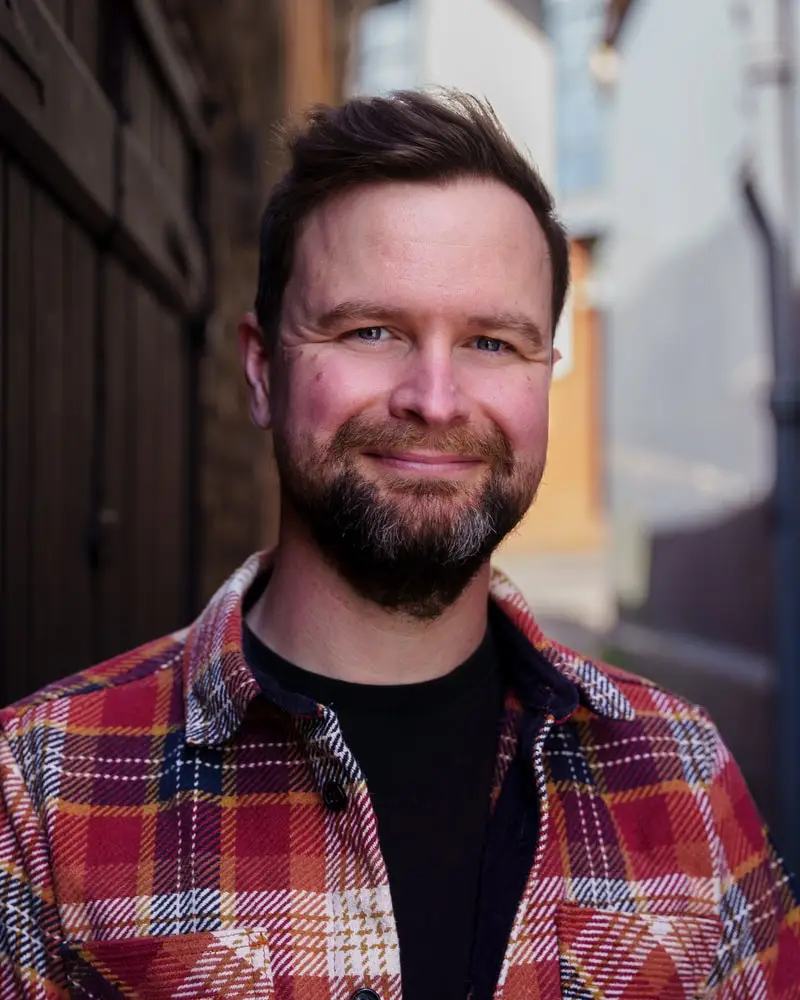 Alan in a red checked overshirt, smiling, in a narrow brick alley